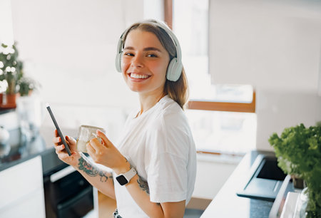 A Cheerful and Joyful Young Woman Experiencing Enjoyable Music in a Modern Kitchen Settingの写真素材