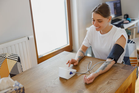 A woman is performing a blood pressure measurement at home using a digital monitor deviceの写真素材