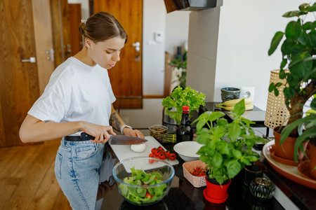 A woman is diligently cooking a fresh salad in a modern kitchen, surrounded by vibrant herbsの写真素材