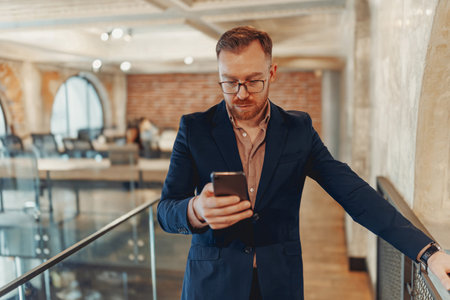 A Professional Man Utilizing a Smartphone in a Contemporary Office Space Environmentの写真素材