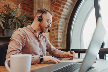 A Focused Man Working Remotely Enthusiastically with Headphones and His Laptop in a Modern Setting
