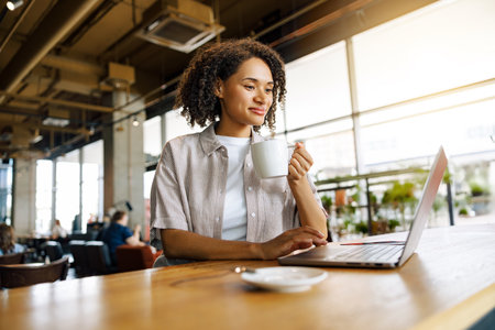 A Focused Woman Deeply Engaged in Her Work on a Laptop While Enjoying Coffee in a Modern Cafeの写真素材