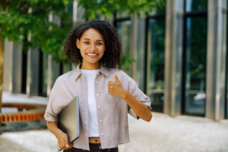 A Confident Young Professional Smiling Happily Outdoors While Using a Laptop for Workの写真素材