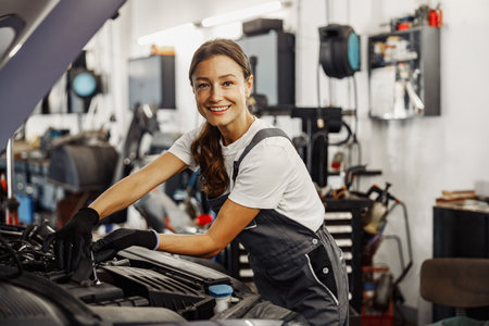 A skilled female mechanic diligently working on a car engine in a modern workshop environmentの写真素材