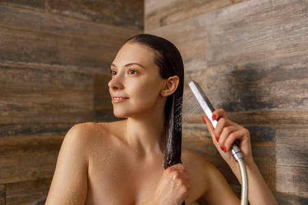 A beautiful woman confidently styling her hair in a modern and refreshing shower settingの写真素材