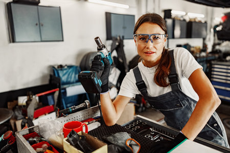 Dedicated Female Mechanic Working in a Busy Auto Repair Shop Surrounded by Tools and Equipmentの写真素材