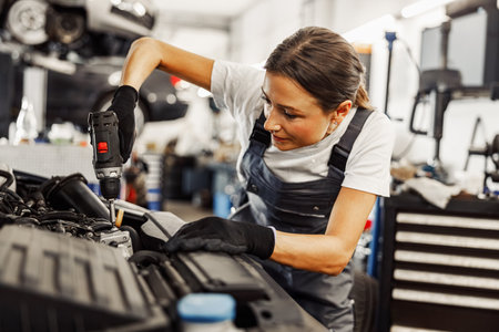 A dedicated female mechanic diligently working on an engine in an auto repair shop environmentの写真素材
