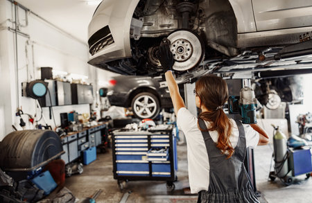 An Automotive Mechanic is diligently working on a car using a lift in the garage environmentの写真素材