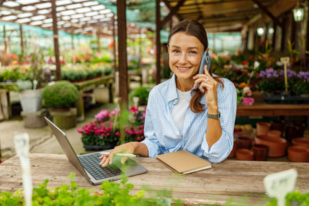 A young professional working diligently in a flower shop while utilizing both a laptop and a phoneの写真素材