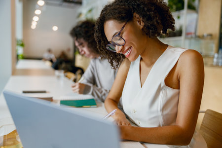 happy worker typing, cheerful professional diligently working using laptop with bright window sceneの写真素材