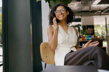 brightly lit woman on call smiles peacefully, relaxed woman by window happily engagingの写真素材