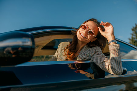 stylish commuter adjusting sunglasses during sunset driveの写真素材