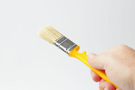Paint brush with a yellow handle in the hand of a worker, close-up, white background.