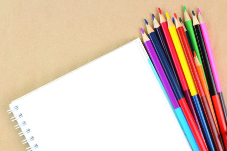 Colored pencils and sketchbook on the desktop. School or education theme concept. Top view, flat...