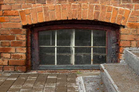 A window in the basement of an old brick building and a concrete staircase.の写真素材