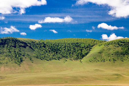Landscape with green hills and a bright blue sky with clouds.