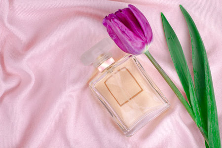 Spring tulip and bottle with perfume on a background of pink fabric with waves and folds, top view.