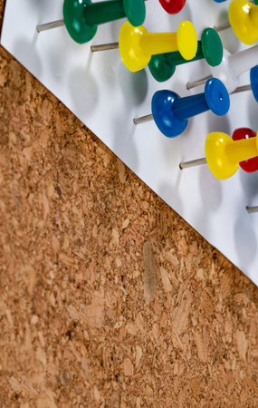 Different colored pushpins stuck into a reminder or note sheet on a cork office board