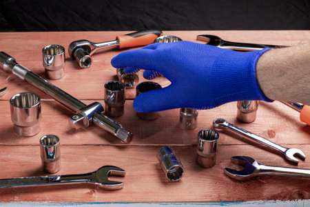 The hand of the foreman in a blue work glove takes a wrench from the work table.