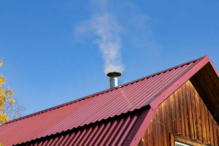 Steel roof of a private house with chimney and smoke against the backdrop of a beautiful blue sky.の写真素材