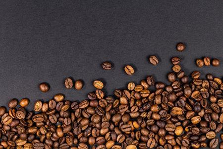 Roasted coffee beans on black texture background, top view, close-up.