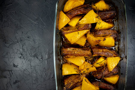 baked pumpkin with pork ribs in a glass form on a black table, top view of a cooked pumpkin with meat, copy spaceの写真素材