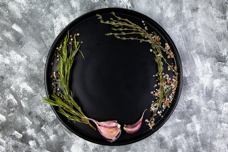 Black round plate with aromatic herbs and spices, on gray, space for text, top view, food photo or menu mockup, flat lay, copy space.の写真素材
