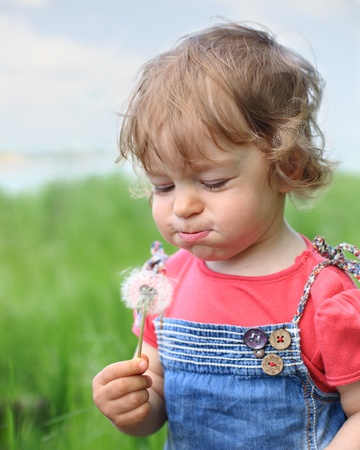 Beautiful child blows on dandelion in the summer. Shallow depth of fieldの写真素材