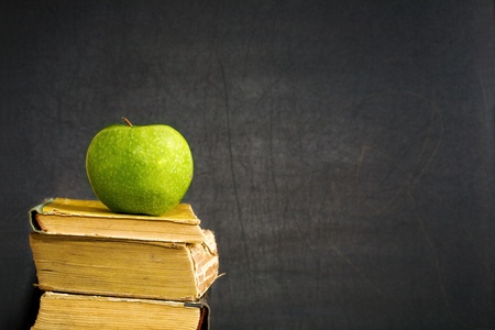 Green apple on old textbook against blackboard with copyspaceの写真素材