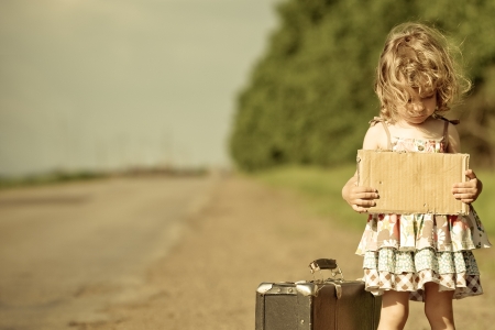 Lonely girl with suitcase standing about road and holding paper with copyspace in handsの写真素材