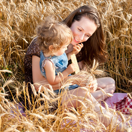 Happy woman and child eating bread in spring wheat fieldの写真素材
