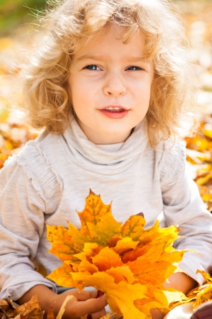 Funny child holding yellow maple leaves in autumn parkの写真素材
