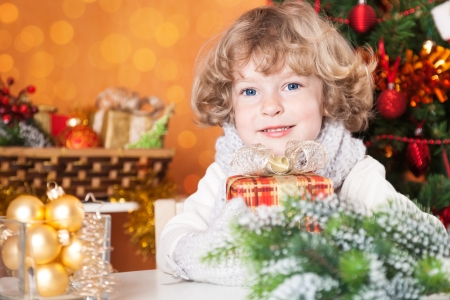 Happy child holding gift box against Christmas tree with decorationsの写真素材