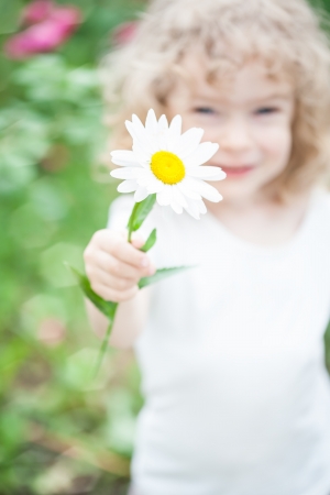 Happy child giving daisy flower against green spring background の写真素材