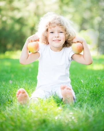 Happy child with apples sitting on green grass in spring park. Healthy lifestyleの写真素材