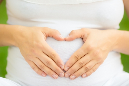 Pregnant woman holding hands on belly in shape of heartの写真素材