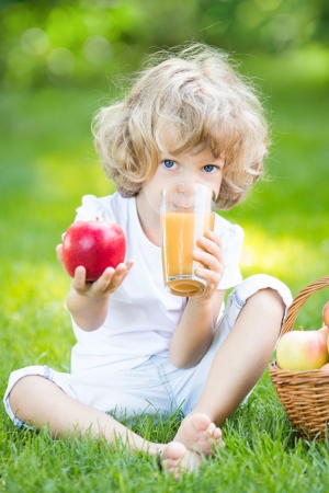 Happy child drinking apple juice in park against green spring backgroundの写真素材