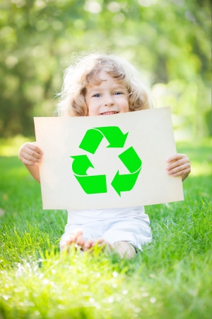 Child holding paper with recycle symbol against green spring background. Ecology conceptの写真素材