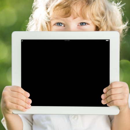 Happy child holding tablet PC outdoors in spring parkの写真素材