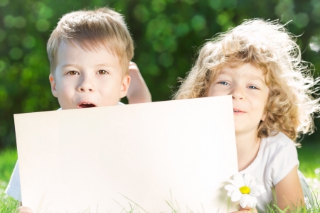 Happy children with paper blank lying on green grass in spring parkの写真素材
