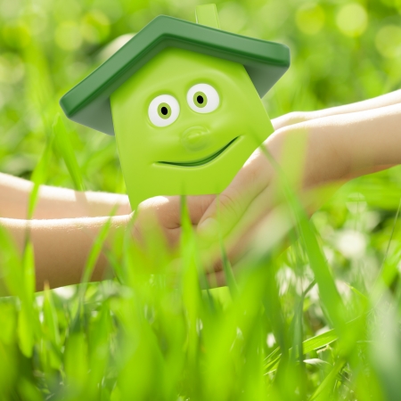 Eco cartoon house in hands against spring green background  Family home conceptの写真素材