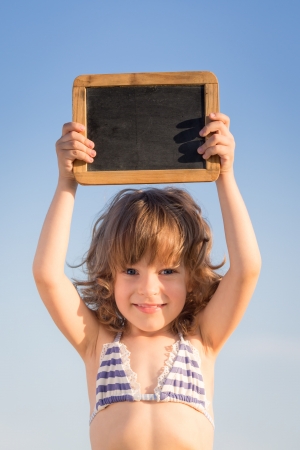 Happy child holding blank blackboard against blue sky backgroundの写真素材