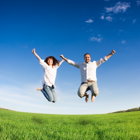 Happy couple jumping in green field against blue sky Summer vacation concept Happy couple jumping in green field against blue sky Summer vacation concept