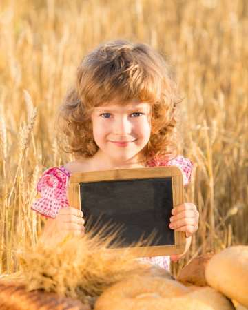 Happy child with bread in yellow autumn wheat field  Kid holding blackboard with copyspaceの写真素材