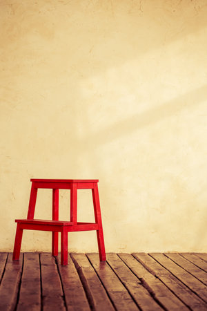 Red chair in empty room interior with grunge concrete wall and wooden floor