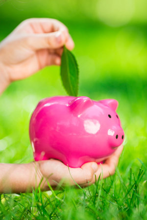 Piggybank and leaf in hands against green spring background. Shallow depth of fieldの写真素材