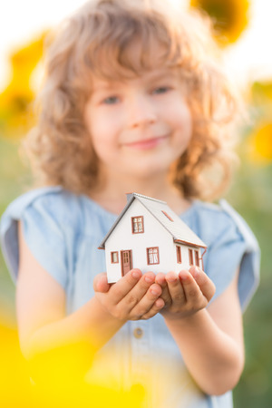 Child holding house in hand against spring flower background. Real estate conceptの写真素材