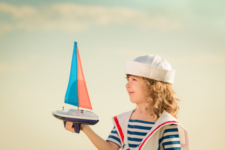 Happy kid playing with toy sailing boat against blue sky backgroundの写真素材