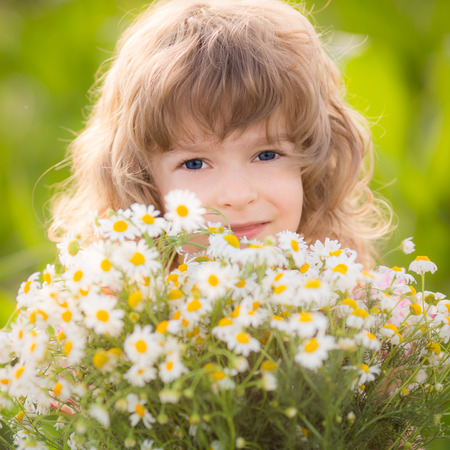 Happy child with daisy flowers outdoors in spring parkの写真素材