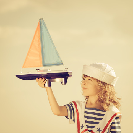 Happy kid playing with toy sailing boat against summer sky background. Travel and vacations conceptの写真素材